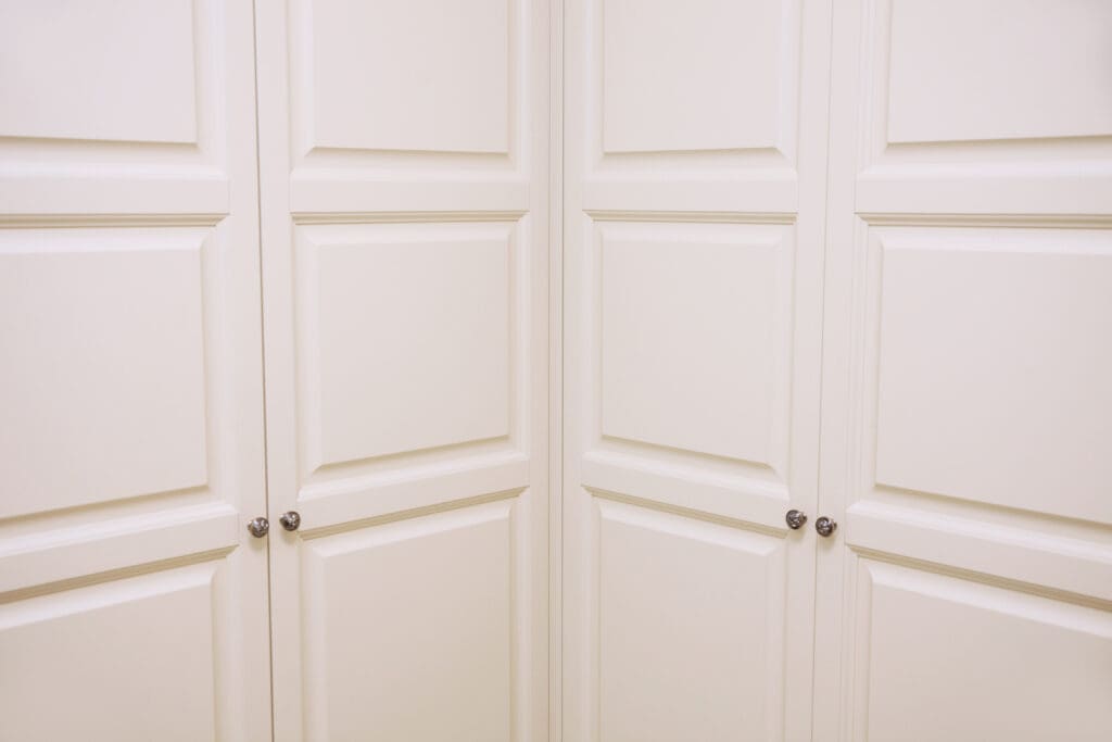 A close-up image of cream-colored cabinet doors with raised-panel detailing. The cabinets have small round metal knobs, and the doors are flush with each other, creating a seamless appearance.