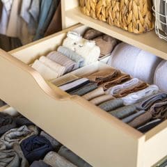 A well-organized closet drawer is shown, featuring neatly folded clothing items. The top drawer holds various socks and undergarments, and a woven basket and a wire basket are visible above. The drawer exemplifies efficient and tidy storage.