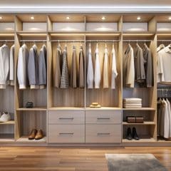 A neatly organized walk-in closet with wooden shelves and cabinets, featuring clothes hung on rods, folded shirts and sweaters, baskets, and neatly arranged shoes. The closet is well-lit with LED lights, creating a warm ambiance.