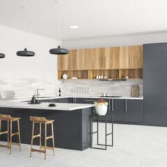 A modern kitchen with black and wood cabinetry, white countertops, and an island with three wooden stools. The backsplash consists of light gray tiles, and three black pendant lights hang above the island. Built-in ovens and shelves with decor are on the right.