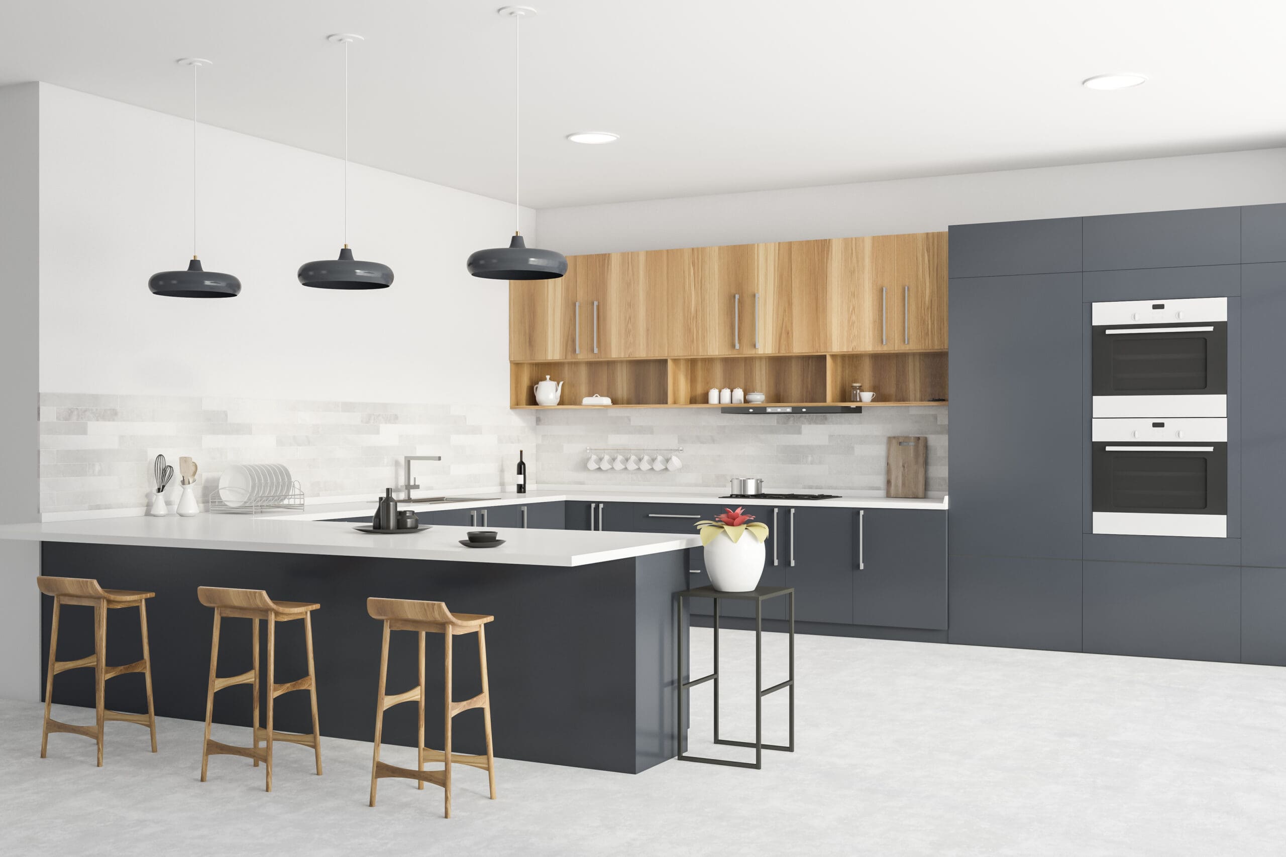 A modern kitchen with black and wood cabinetry, white countertops, and an island with three wooden stools. The backsplash consists of light gray tiles, and three black pendant lights hang above the island. Built-in ovens and shelves with decor are on the right.