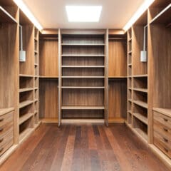 A spacious walk-in closet with wooden shelves, drawers, and hanging spaces on both sides. Bright lighting illuminates the closet, highlighting the wood grain and organized layout. A ladder-style shelving unit is centered at the end of the closet.